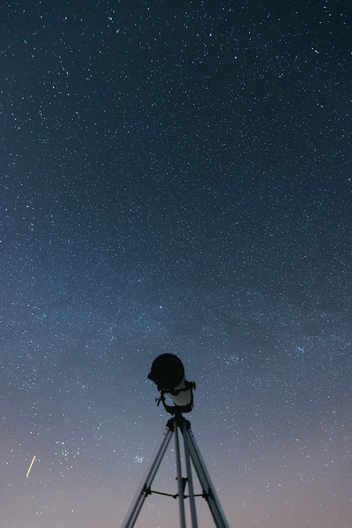 image of a telescope pointing to the night sky . the telescope is a silhouette against the background